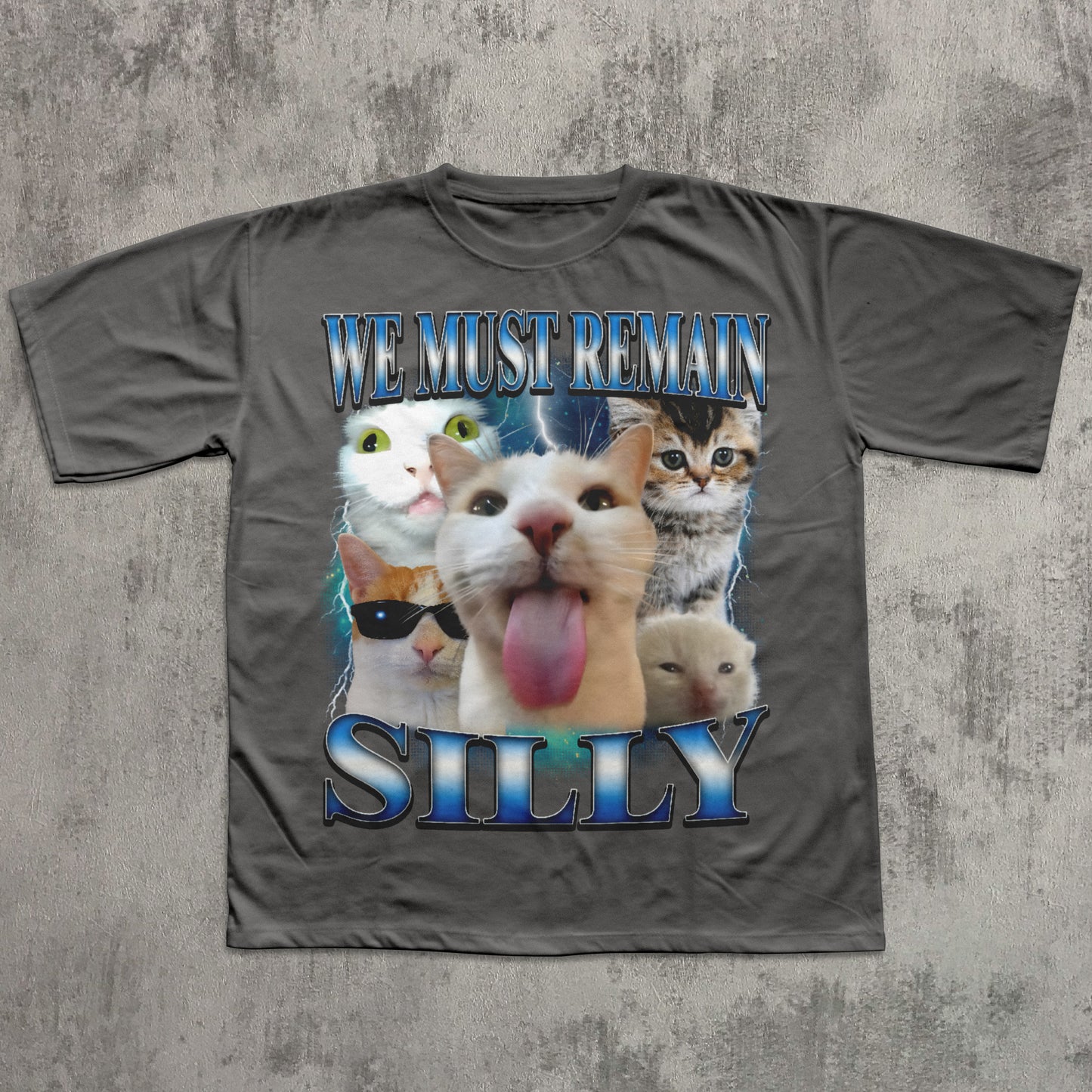 Gray t-shirt with cat-themed design and text 'WE MUST REMAIN SILLY' on a textured gray background