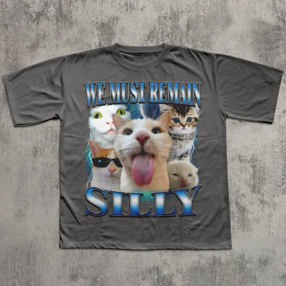 Gray t-shirt with cat-themed design and text 'WE MUST REMAIN SILLY' on a textured gray background