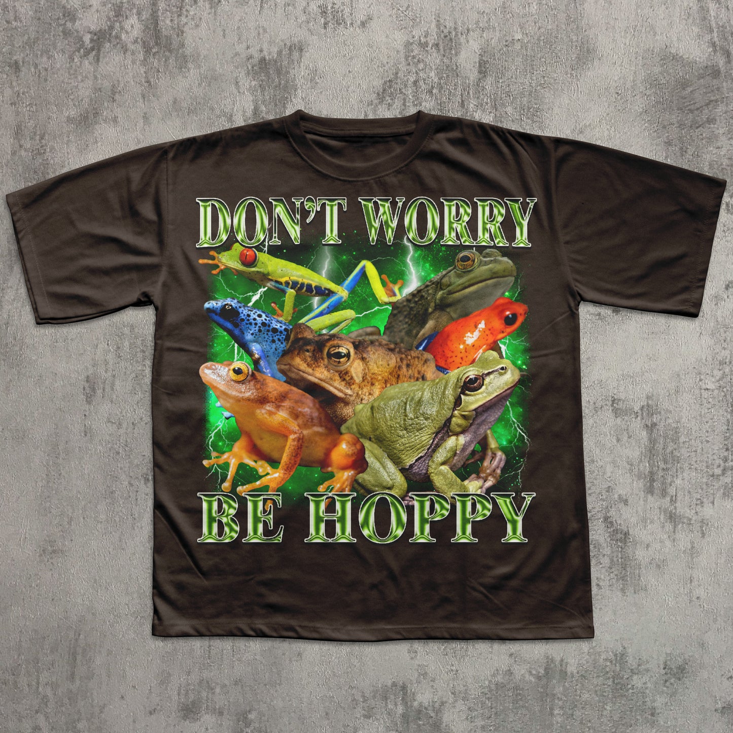 Brown t-shirt with colorful frog design and text 'Don't Worry Be Hoppy' on a concrete background