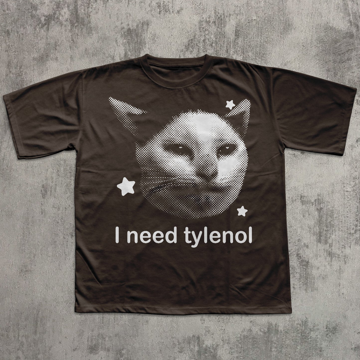 Brown t-shirt with a cat graphic and 'I need tylenol' text on a textured gray background