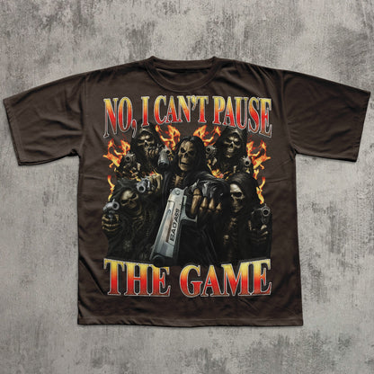 T-shirt with graphic design of skeletons holding guns and text 'No, I Can't Pause The Game' on a concrete background
