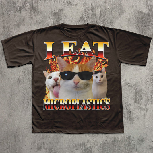 T-shirt with a graphic of cats wearing sunglasses and text 'I Eat Microplastics' on a concrete background