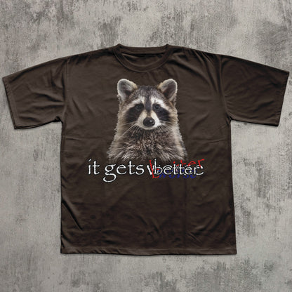 Brown t-shirt with a raccoon graphic and text 'it gets better' on a textured gray background