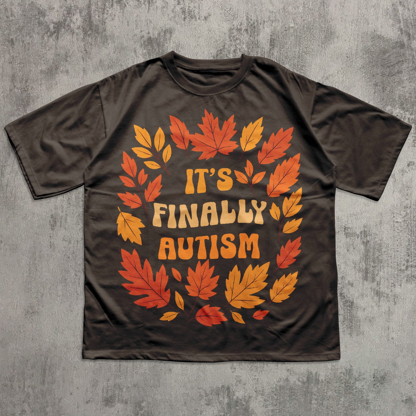 Brown t-shirt with autumn leaf design and 'It's Finally Autism' text on a gray textured background