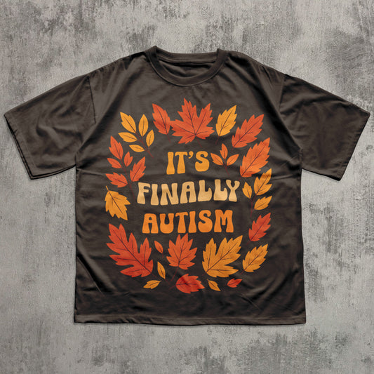 Brown t-shirt with autumn leaf design and 'It's Finally Autism' text on a gray textured background