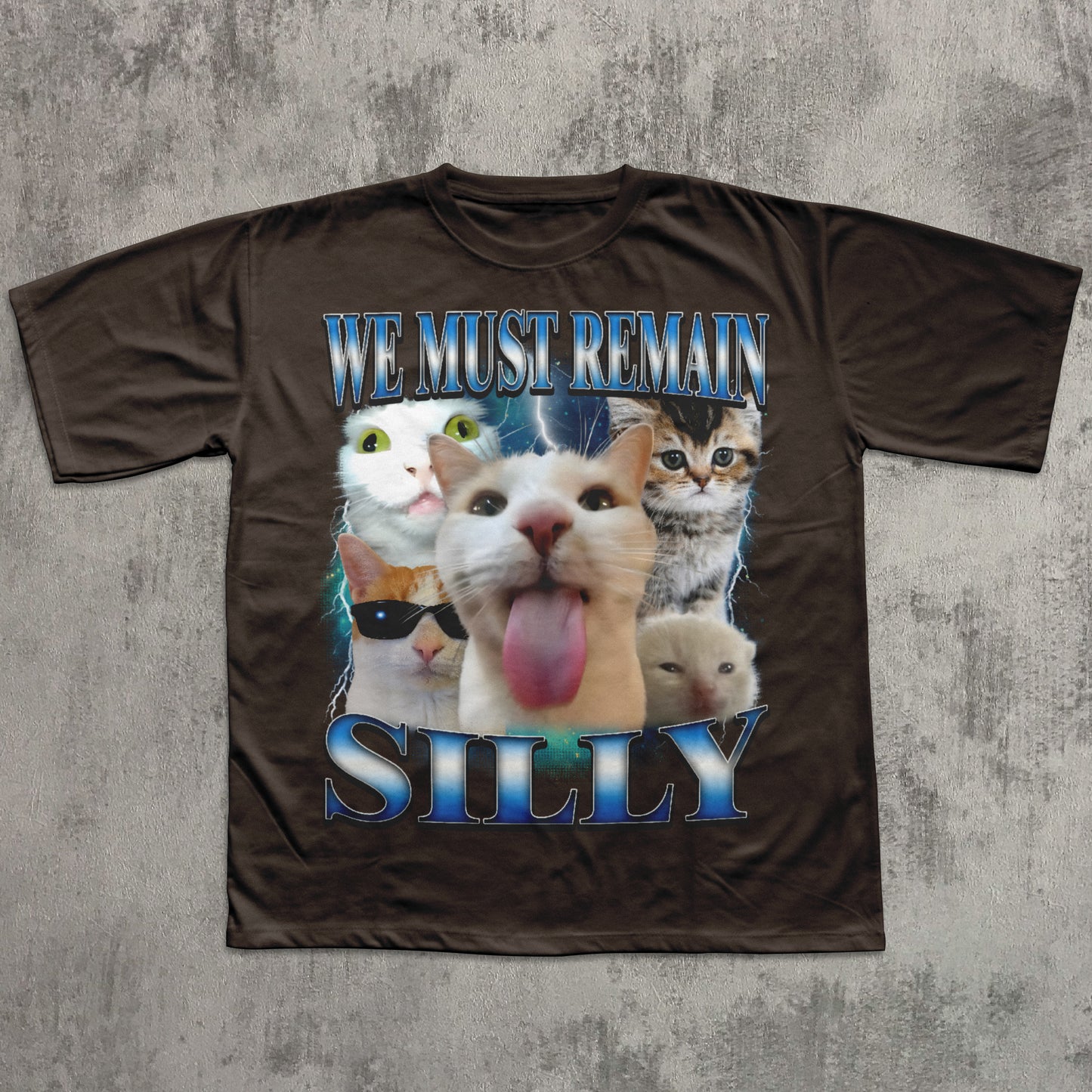 Brown t-shirt with cartoon cats and text 'WE MUST REMAIN SILLY' on a textured gray background