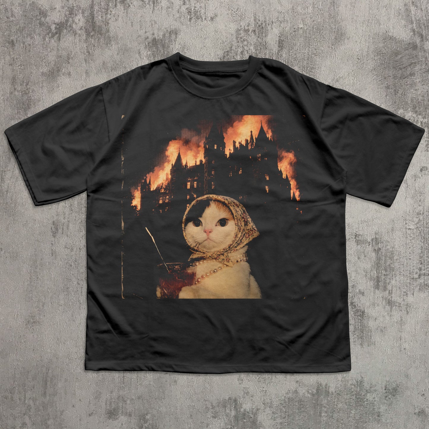 Black t-shirt with a graphic of a cat in a hood and a castle on fire, on a textured gray background.