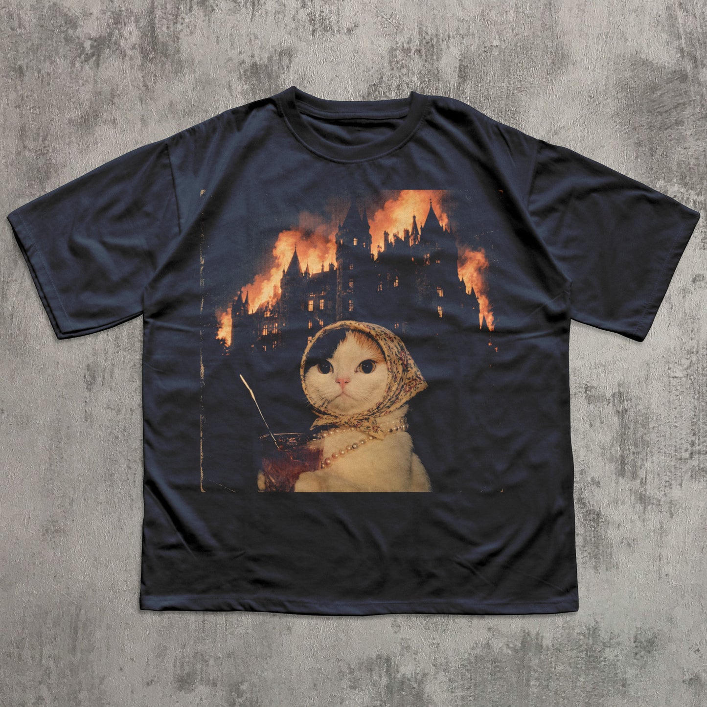 Black t-shirt with a graphic of a cat in a hood and castle on fire design, on a textured gray background.