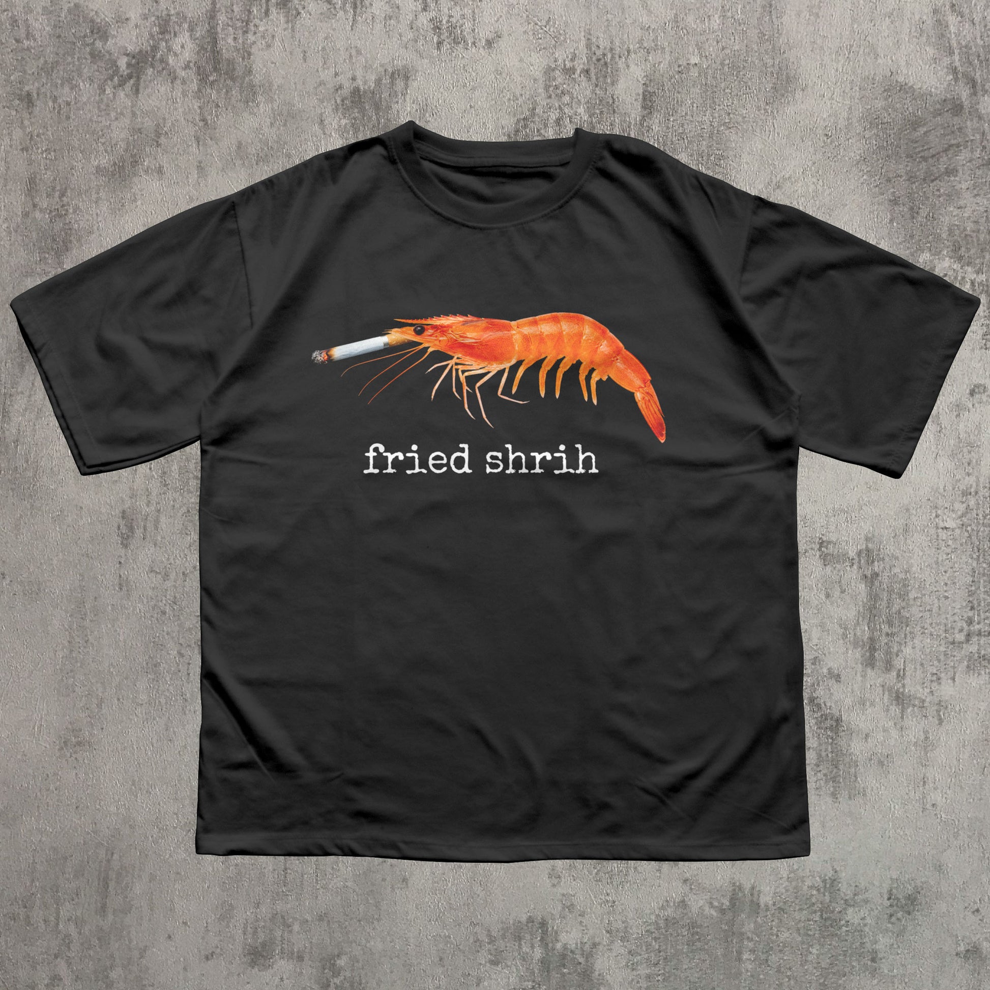 Black t-shirt with a shrimp smoking a cigarette graphic and 'fried shrim' text on a concrete surface.