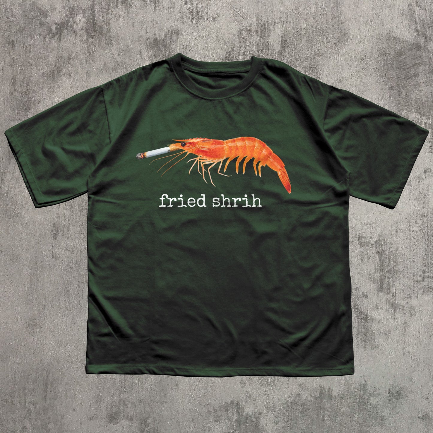 Green t-shirt with a shrimp smoking a cigarette graphic and 'fried shrim' text on a concrete surface.