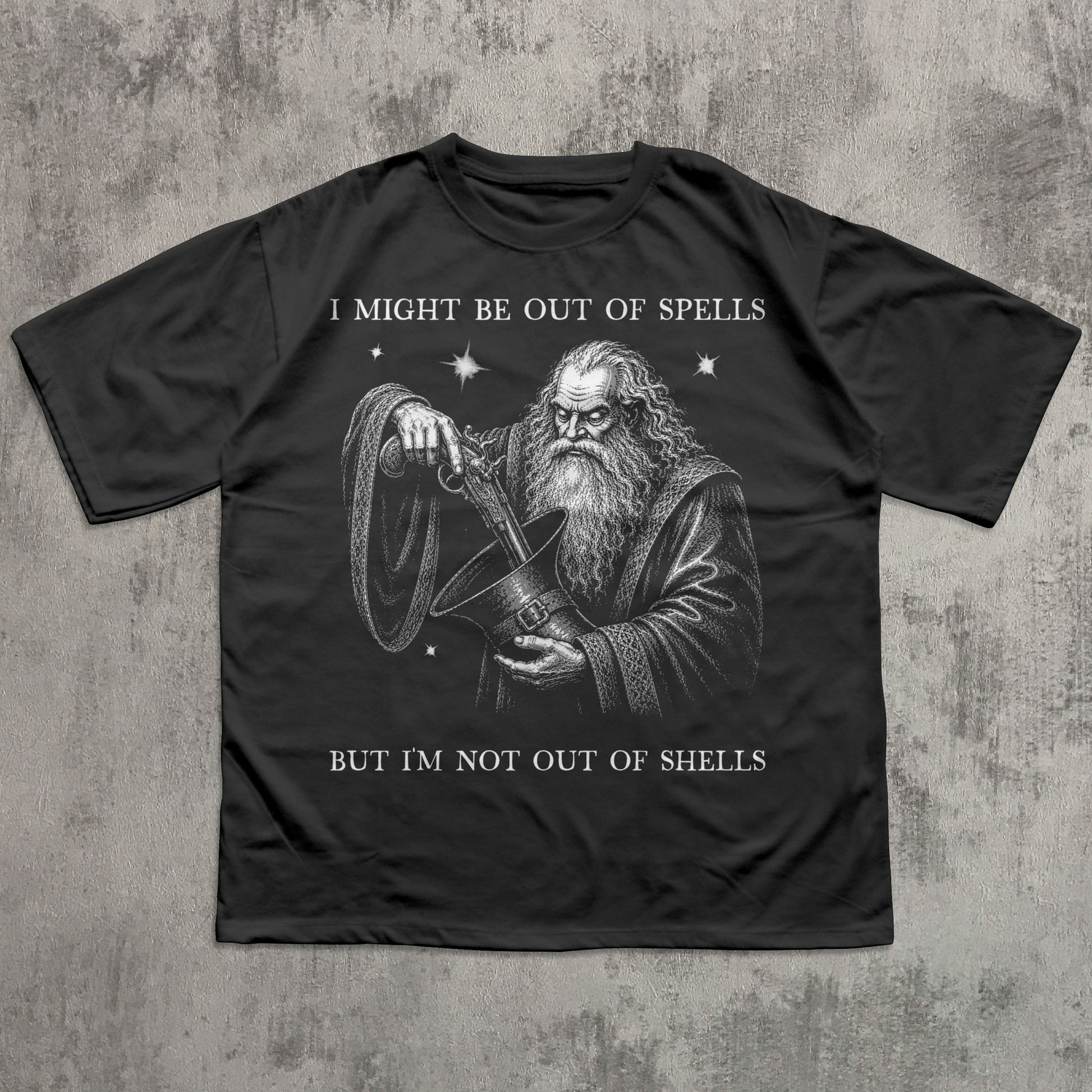 A black short-sleeve t-shirt with a white graphic print of a wizard holding a shell, with the text 'I MIGHT BE OUT OF SPELLS BUT I'M NOT OUT OF SHELLS' on a textured gray background.