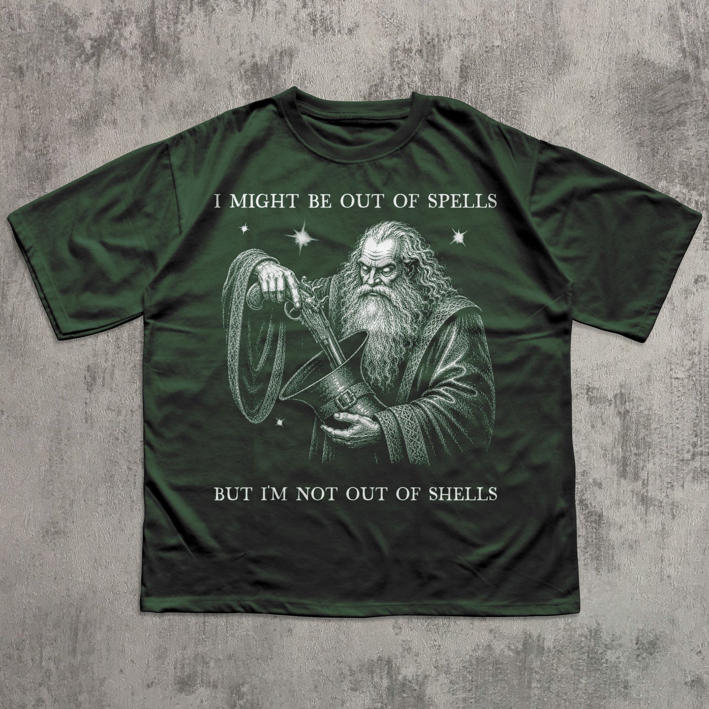 A dark forest green short-sleeve t-shirt with a graphic of a wizard holding a shell, accompanied by the text 'I MIGHT BE OUT OF SPELLS BUT I'M NOT OUT OF SHELLS' in white, laid flat on a textured gray background.