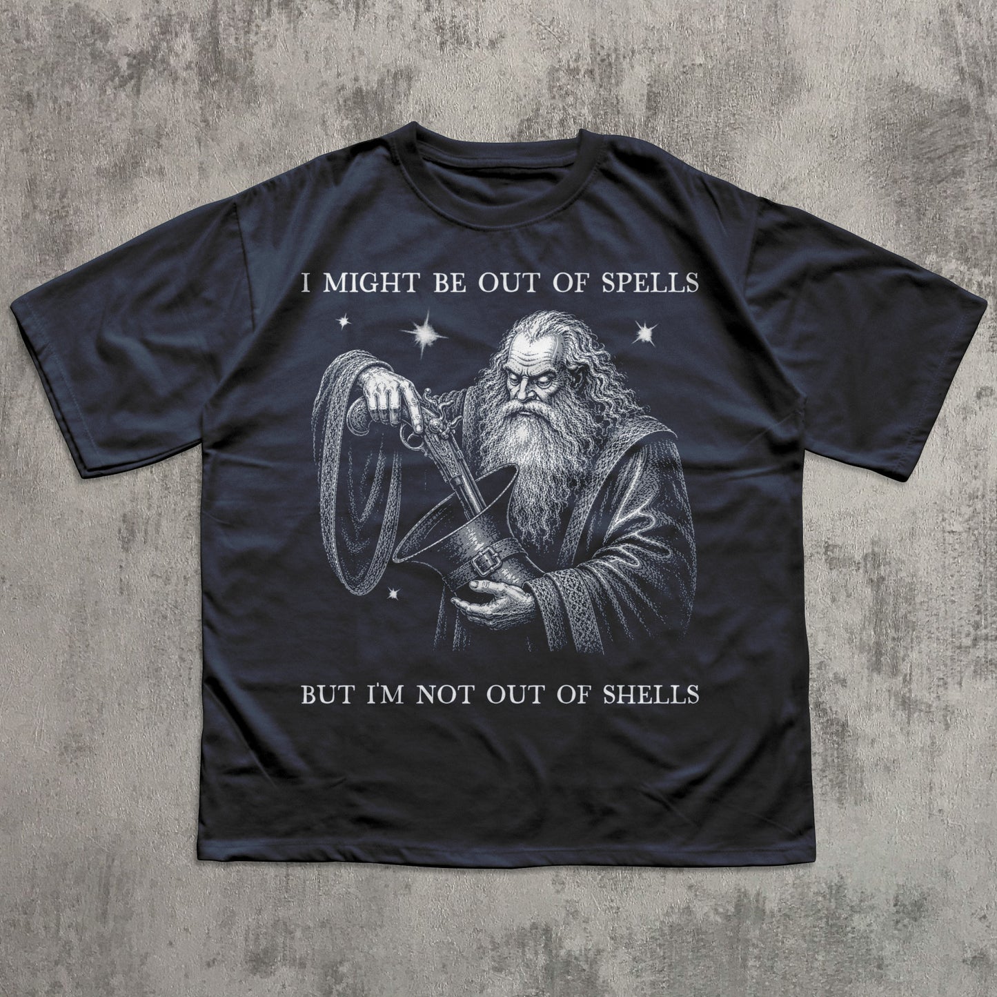 A black graphic t-shirt featuring an illustration of a wizard holding a shell, with the text 'I MIGHT BE OUT OF SPELLS BUT I'M NOT OUT OF SHELLS' printed in white. The t-shirt is laid flat on a textured gray concrete background.