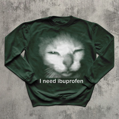 Unisex green crewneck sweatshirt with halftone sad cat meme graphic and humorous slogan ‘I need ibuprofen,’ perfect for cat lovers and meme apparel