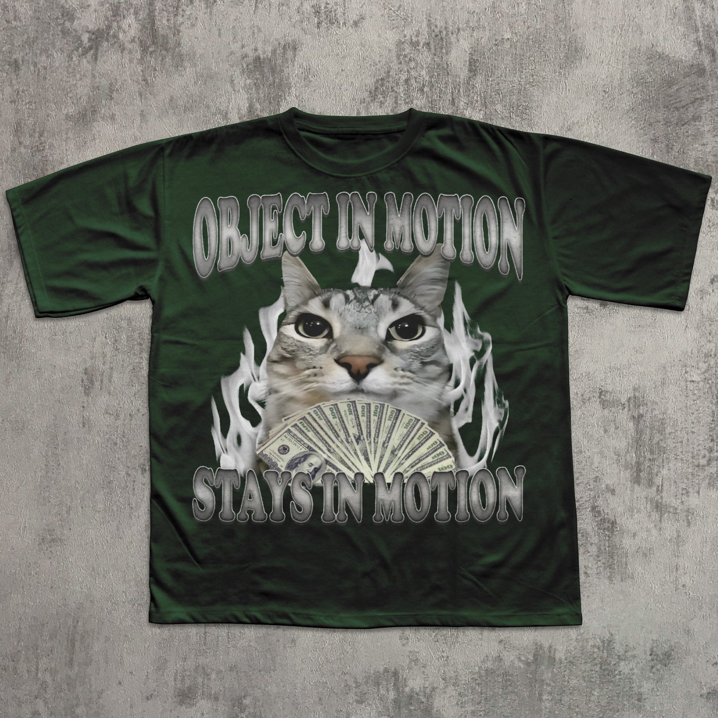 Green t-shirt with a graphic of a cat holding money and text 'OBJECT IN MOTION STAYS IN MOTION' on a textured gray background.