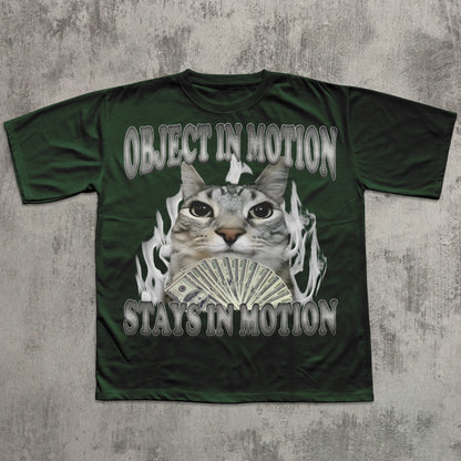 Green t-shirt with a graphic of a cat holding money and text 'OBJECT IN MOTION STAYS IN MOTION' on a textured gray background.
