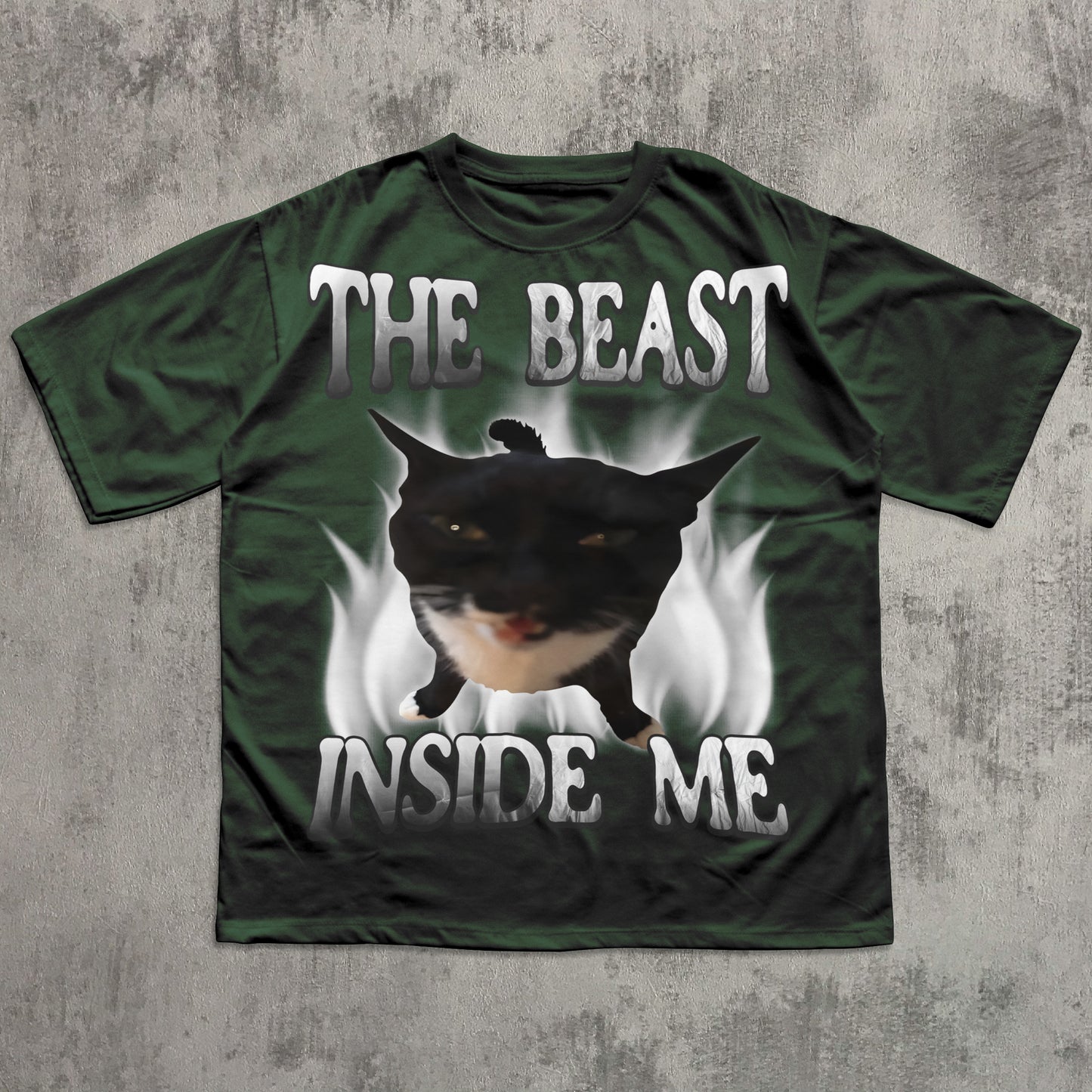 Green t-shirt with a graphic of a cat and text 'The Beast Inside Me' on a concrete surface.