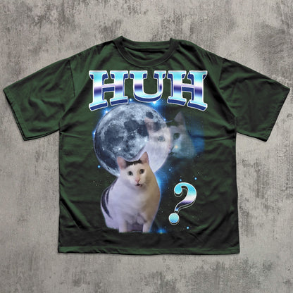 Green t-shirt with a cat graphic and 'HUH?' text on a textured gray background