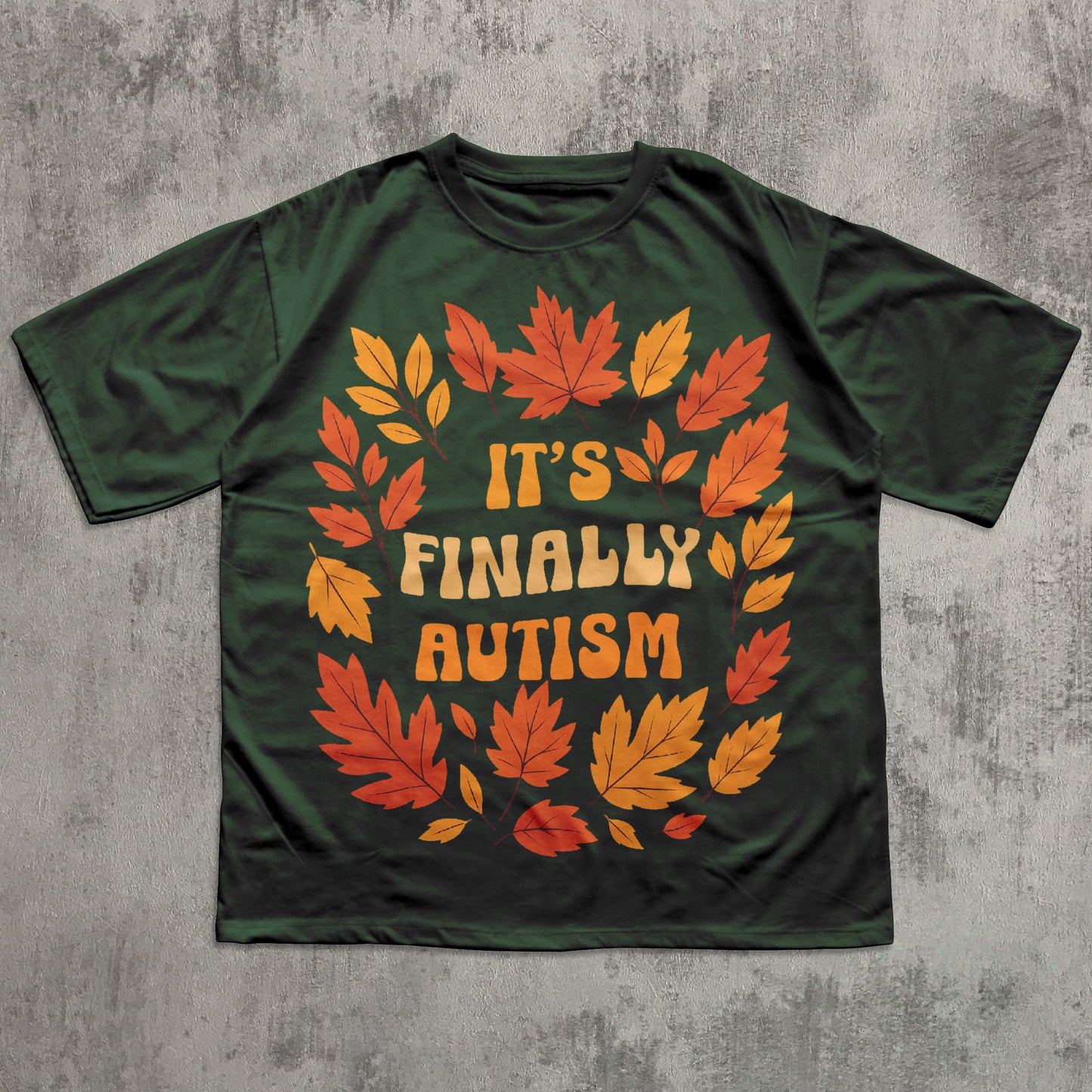 Green t-shirt with autumn leaf design and 'It's Finally Autism' text on a textured gray background