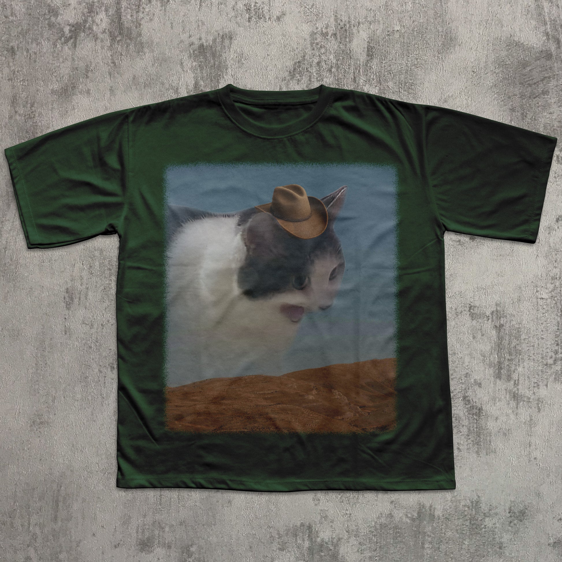 Green t-shirt with a printed design of a cat wearing a cowboy hat on a textured gray background