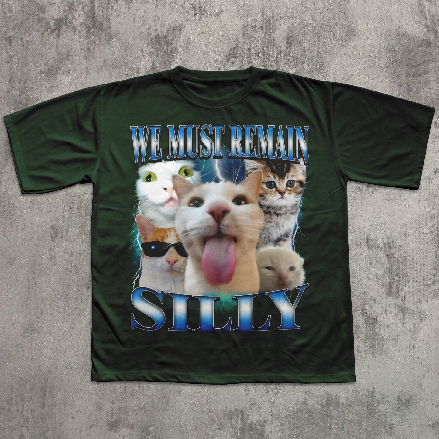 Green t-shirt with cartoon cats and text 'WE MUST REMAIN SILLY' on a textured gray background