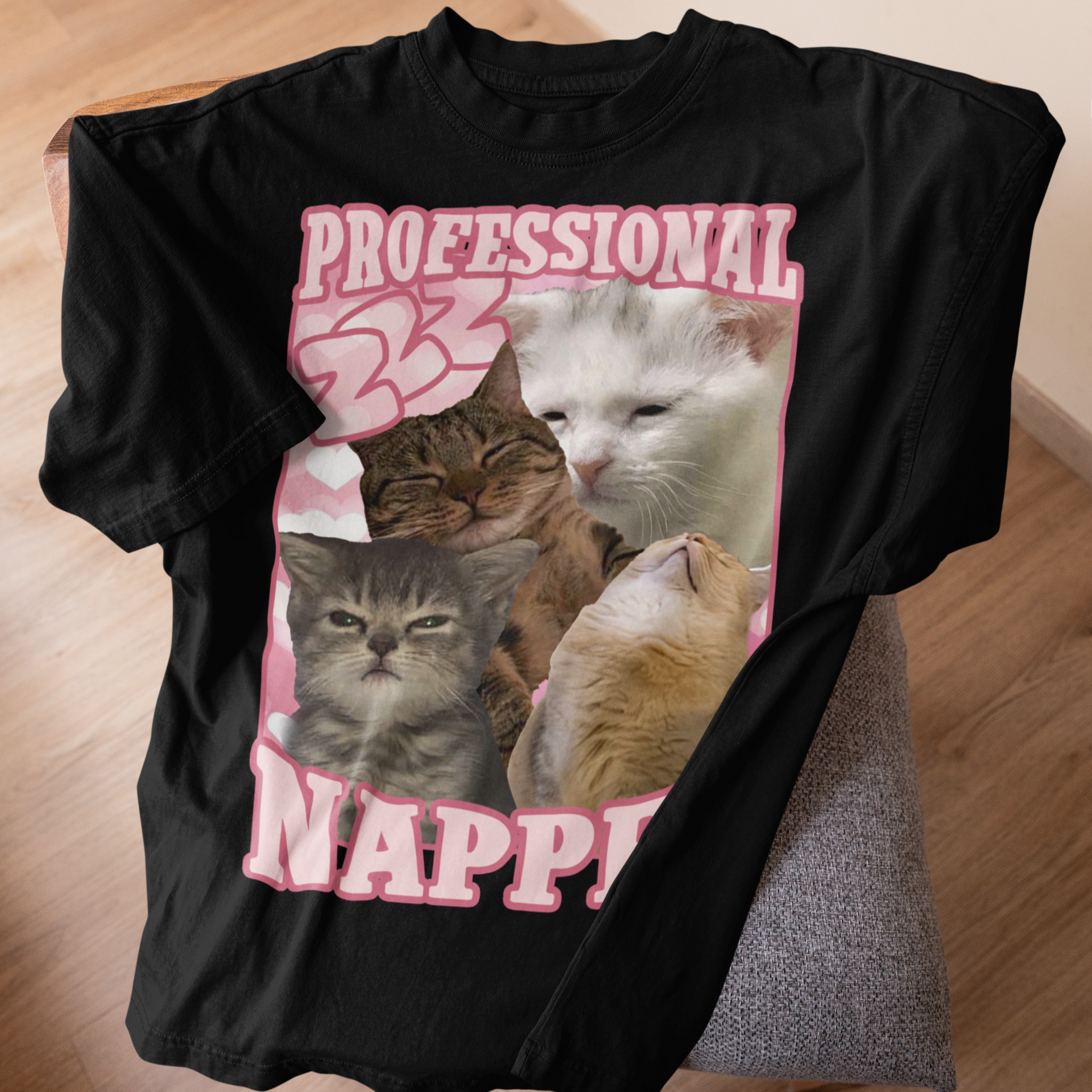 Black t-shirt with a graphic of four cats and the text 'Professional Napper' on a wooden surface.