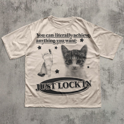 Beige t-shirt with cat graphic and motivational text on a textured gray background