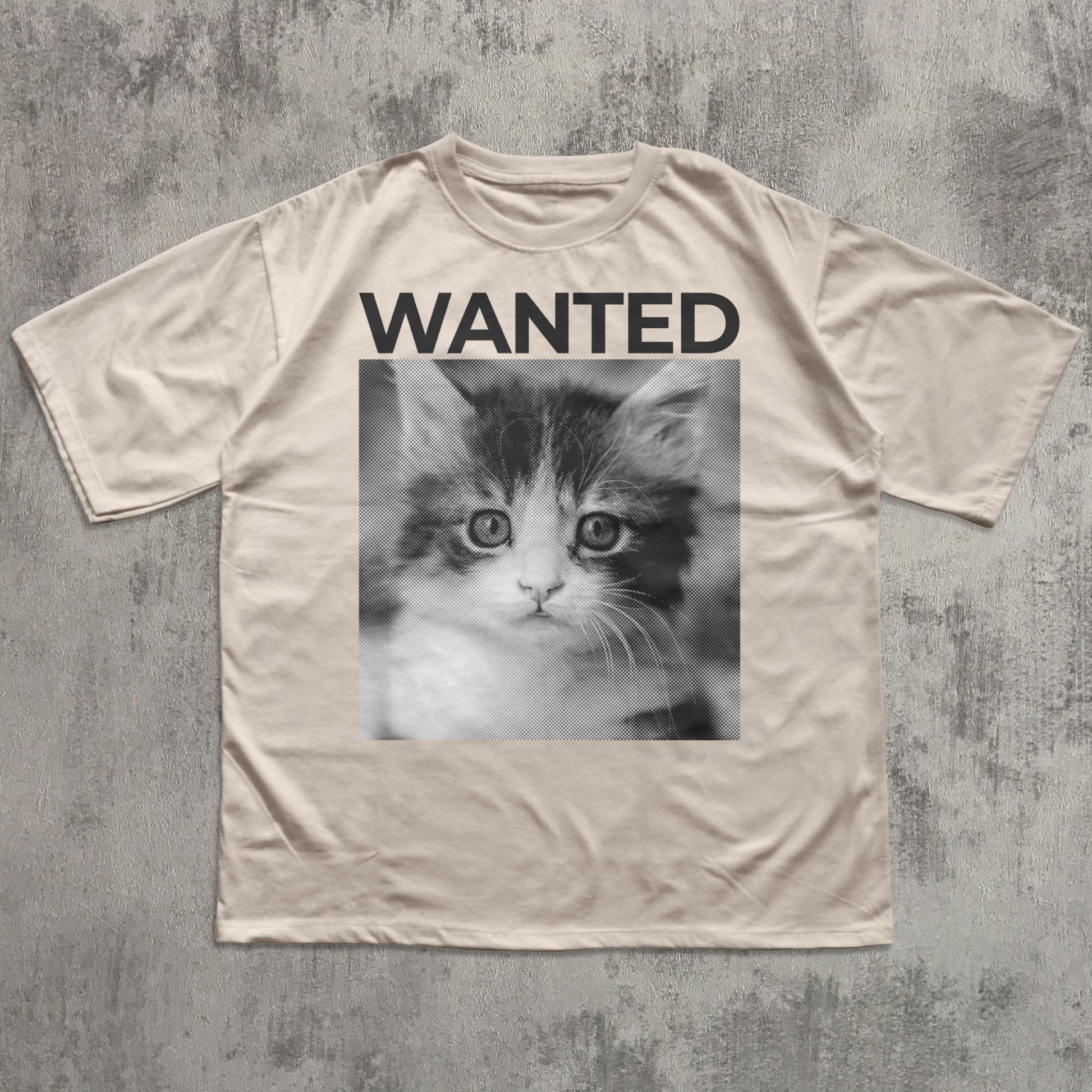 Beige t-shirt with a kitten graphic and 'WANTED' text on a textured gray background