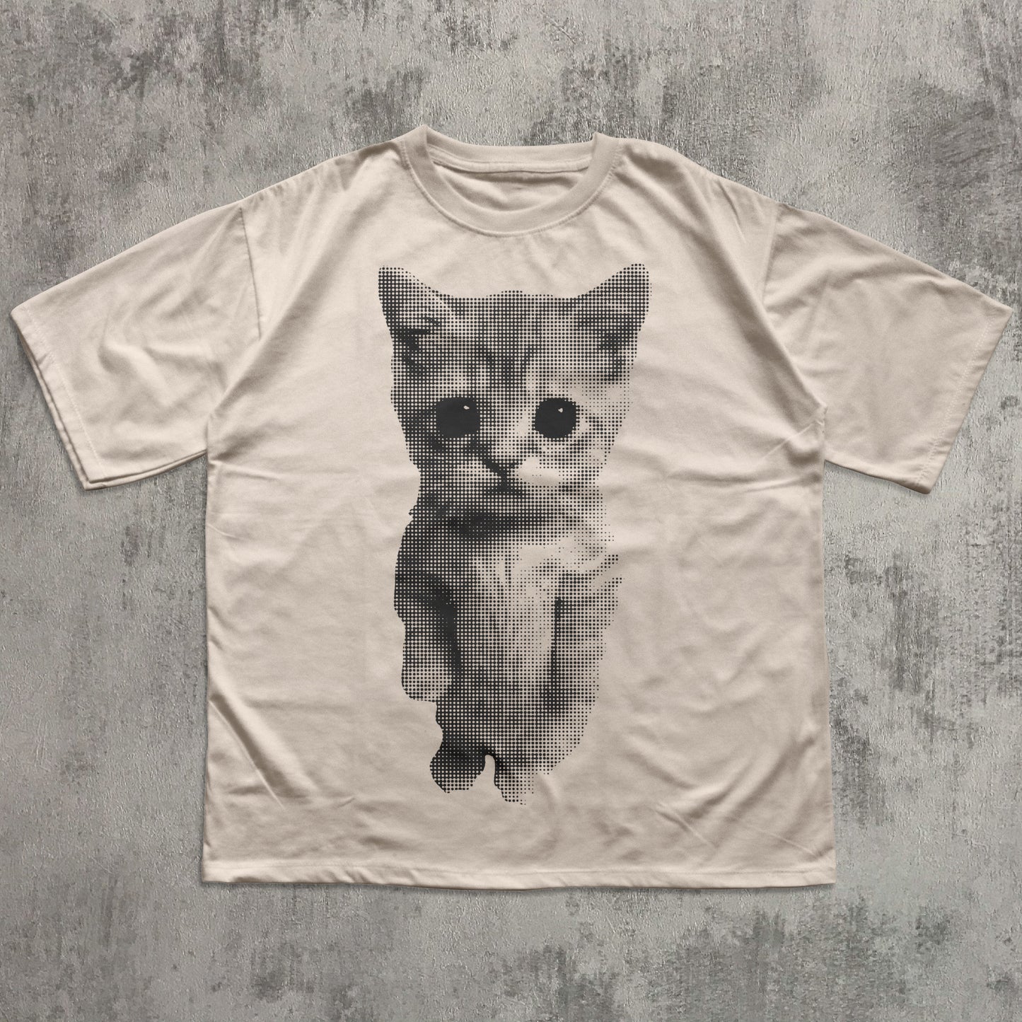 Beige t-shirt with a printed cat design on a textured gray background