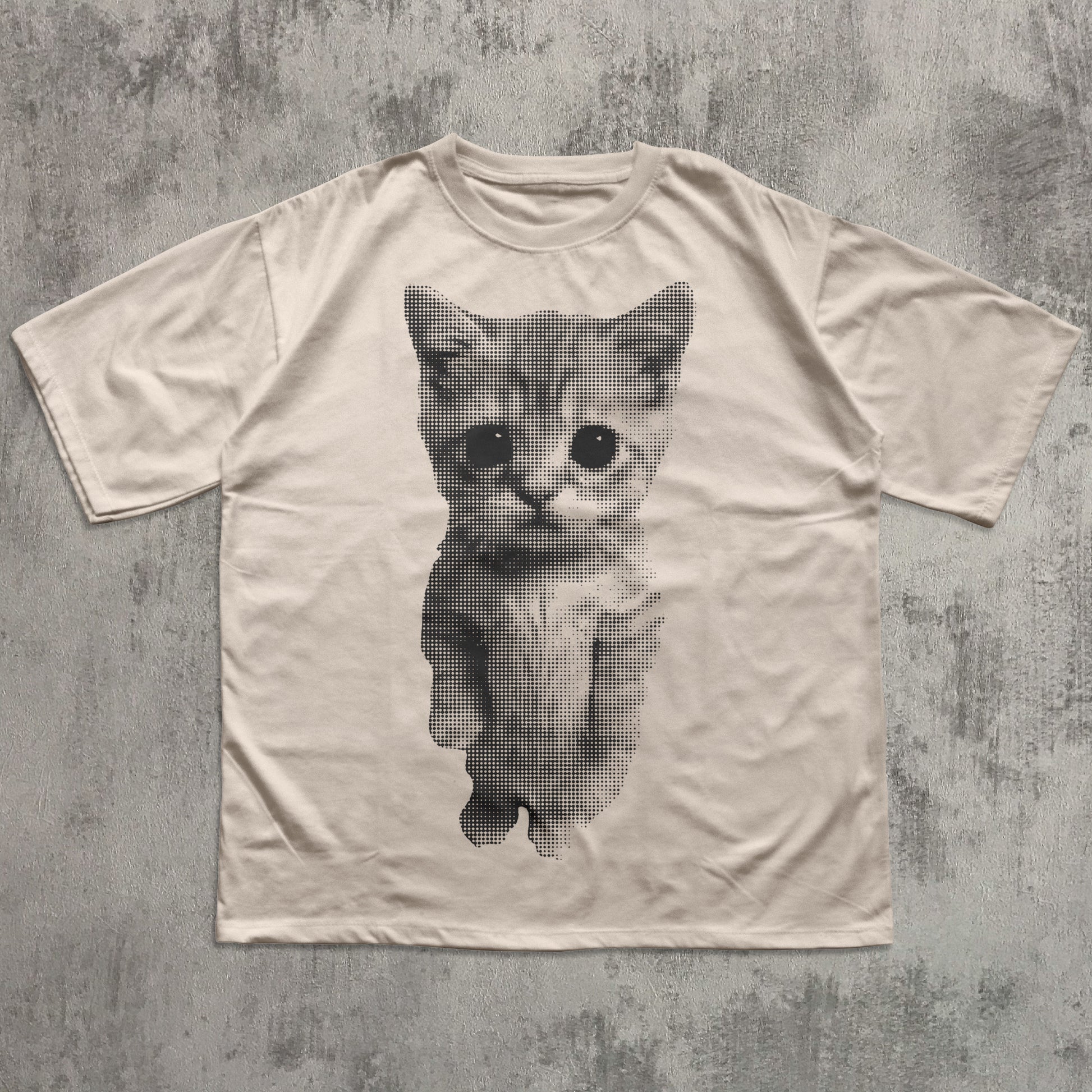 Beige t-shirt with a printed cat design on a textured gray background