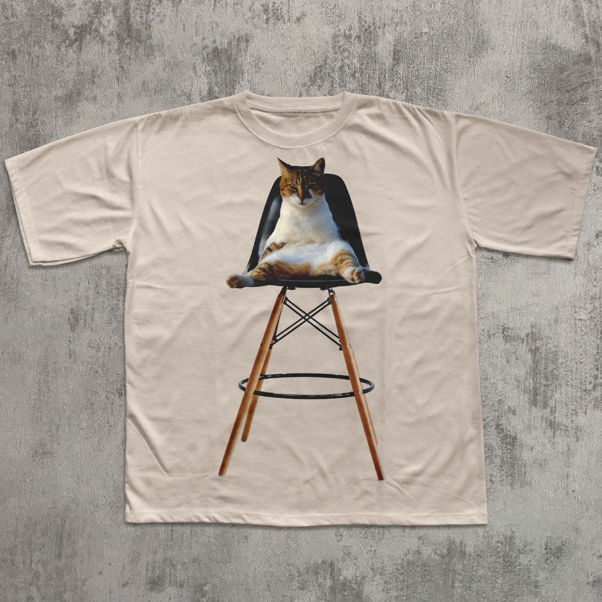 Beige t-shirt with a cat on a stool graphic on a textured gray background
