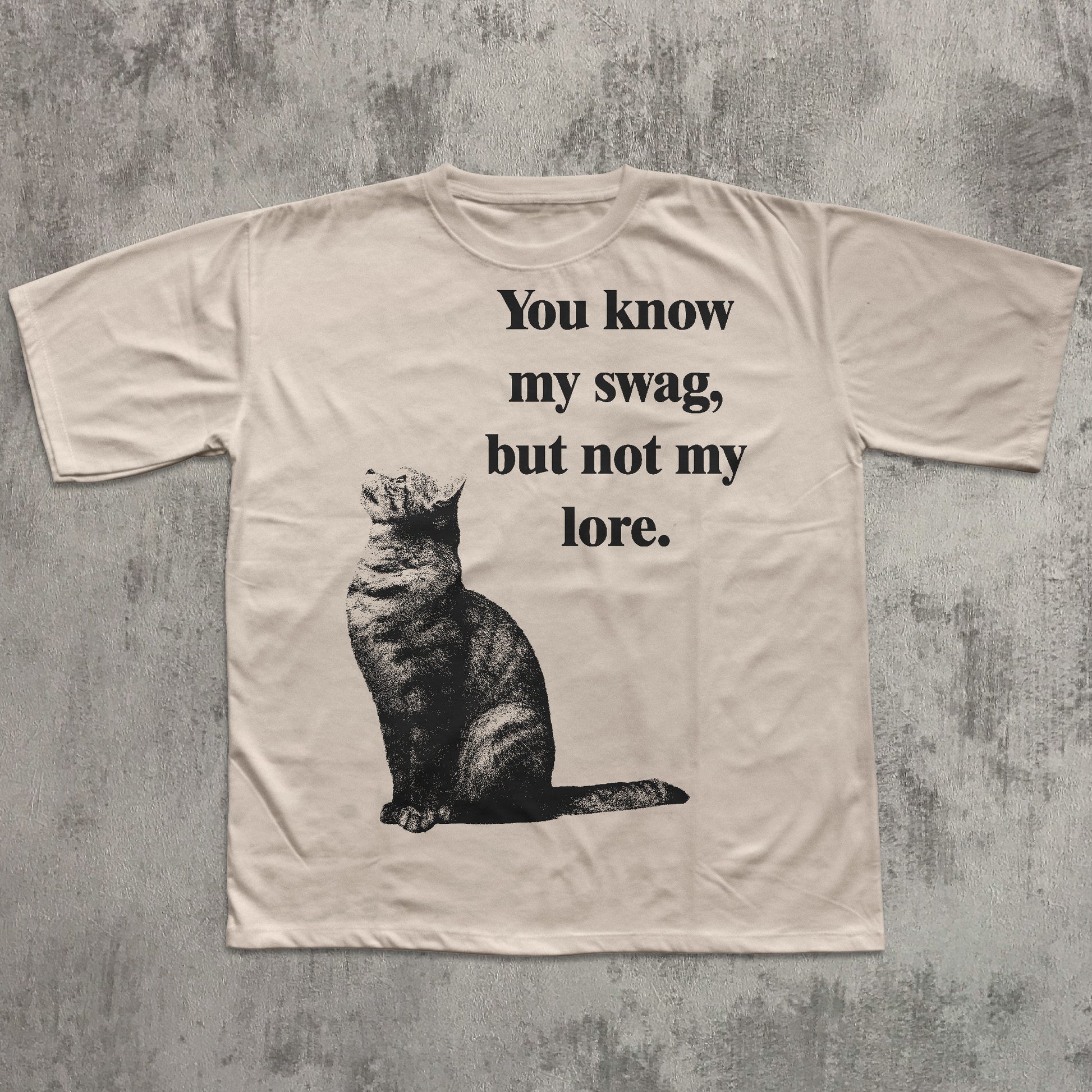 Beige t-shirt with a cat graphic and text on a textured gray background