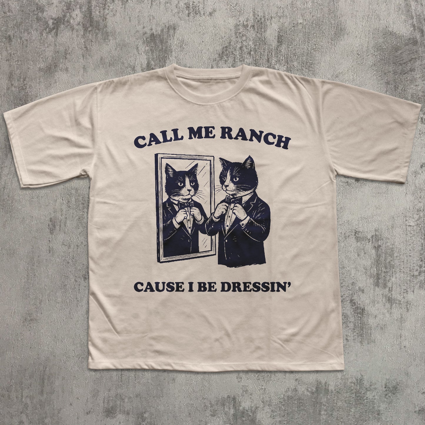 Beige t-shirt with graphic of cats in suits and text 'Call Me Ranch Cause I Be Dressin'' on a textured gray background