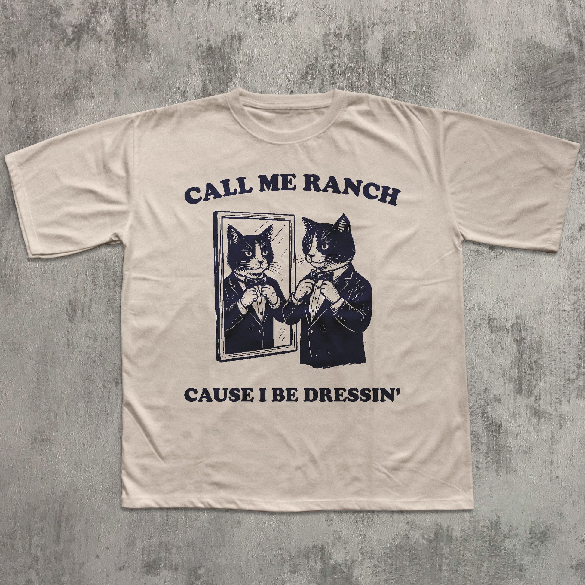Beige t-shirt with graphic of cats in suits and text 'Call Me Ranch Cause I Be Dressin'' on a textured gray background