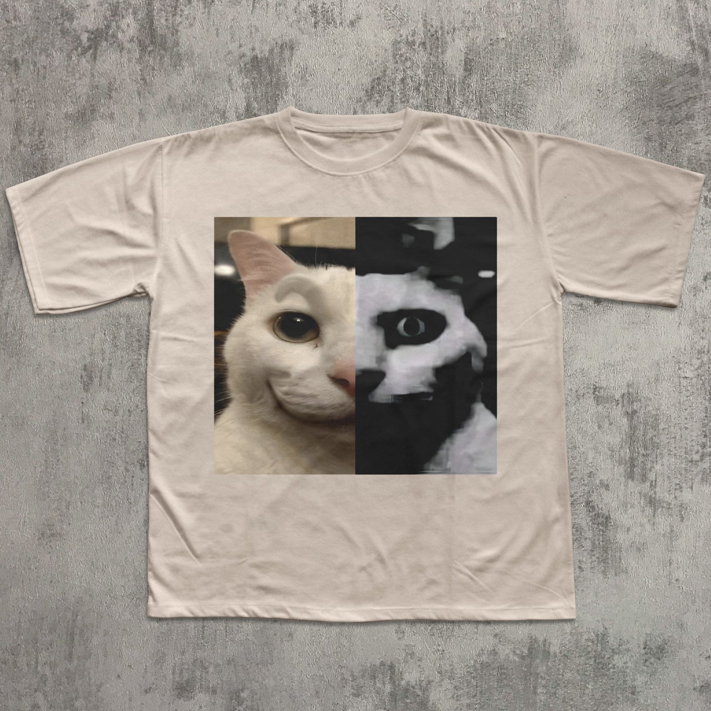 Beige t-shirt with a graphic of a cat's face split in half, one side white and one side black, on a textured gray background.