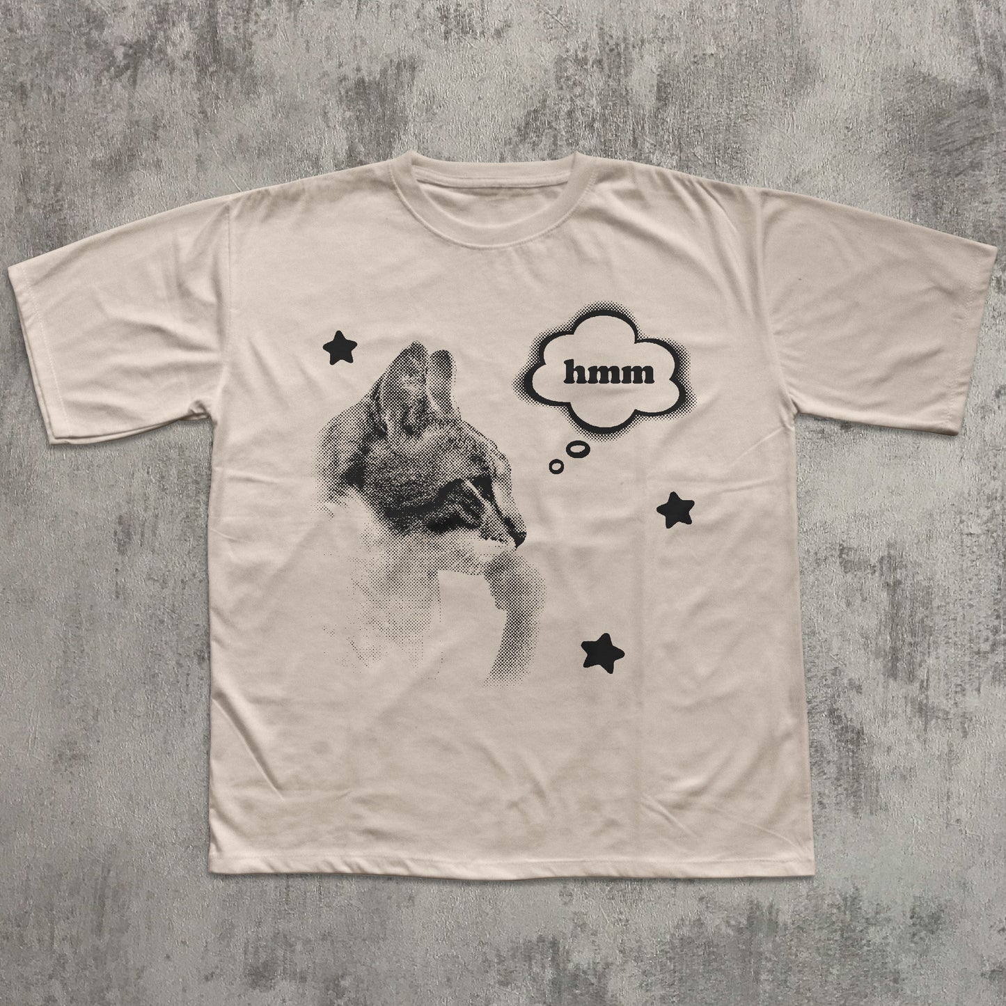 Beige t-shirt with a graphic of a cat and 'hmm' text on a textured gray background