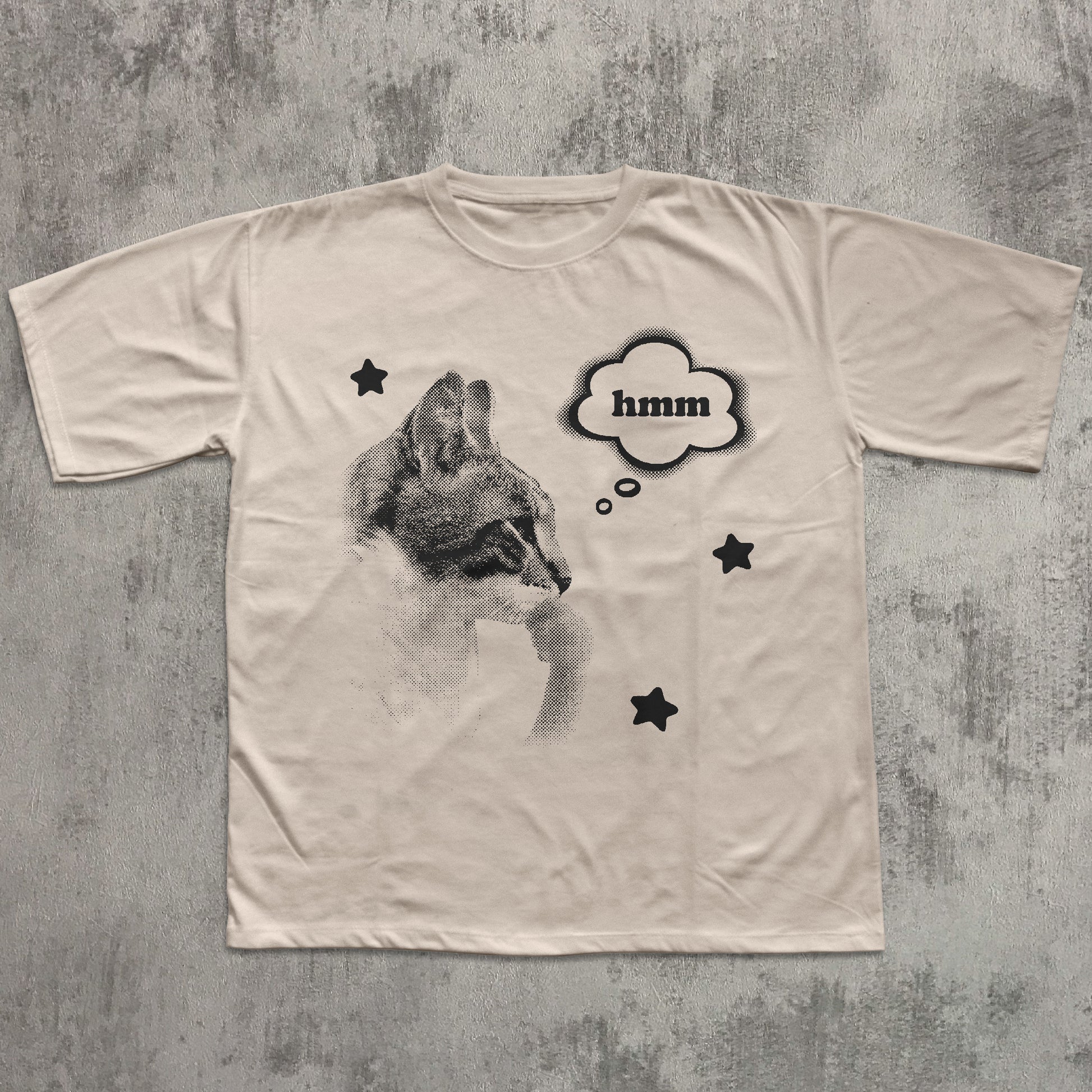 Beige t-shirt with a graphic of a cat and 'hmm' text on a textured gray background