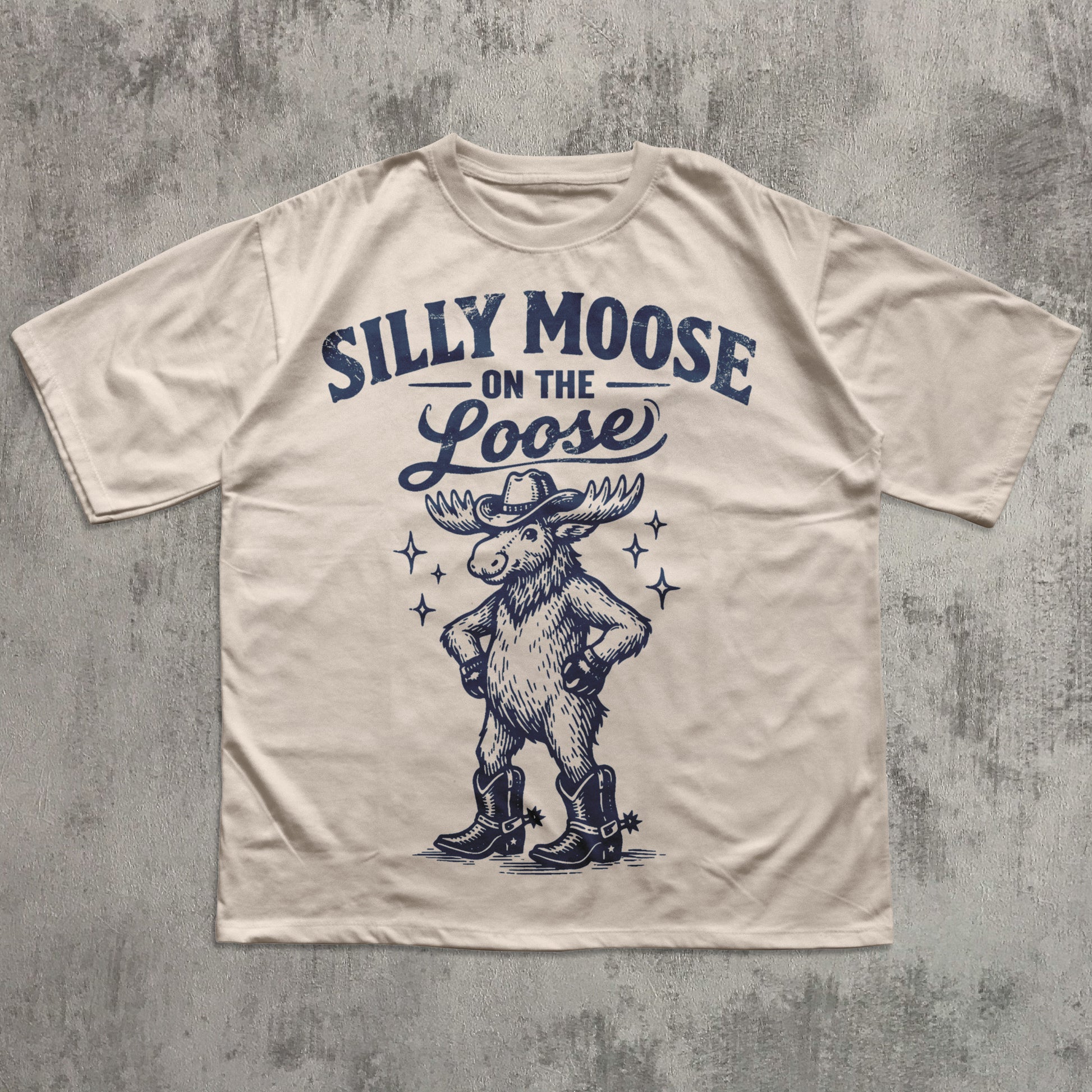 Beige t-shirt with 'Silly Moose on the Loose' graphic and text on a textured gray background