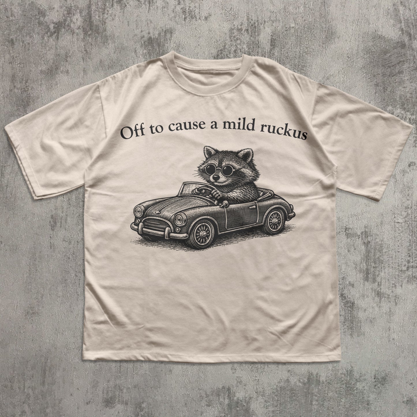 T-shirt with a raccoon driving a car graphic and text on a textured gray background