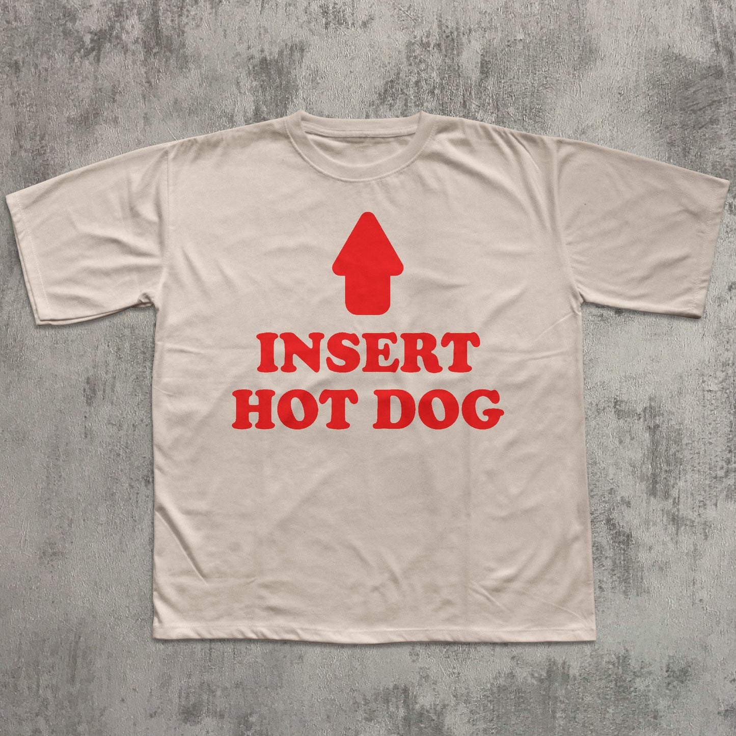 Beige t-shirt with red graphic and text 'Insert Hot Dog' on a textured gray background
