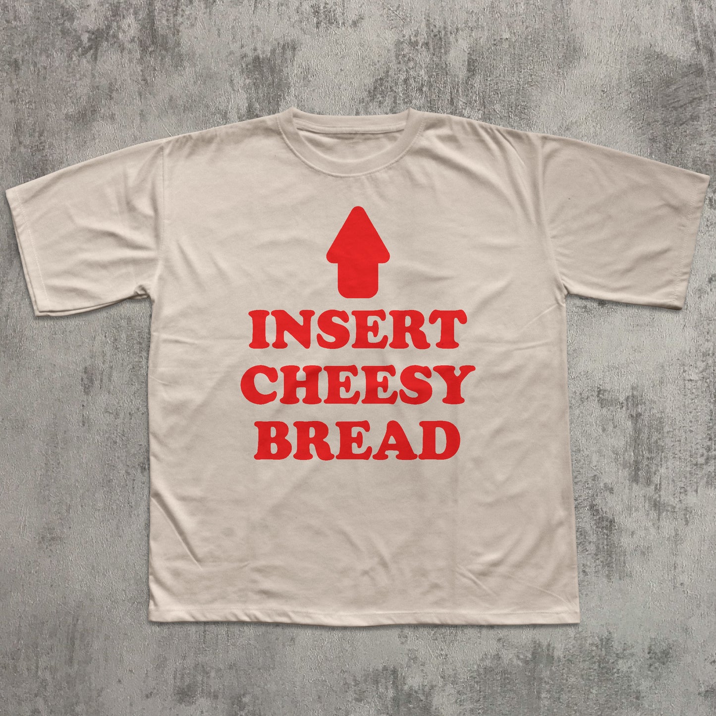 Beige t-shirt with red text and an arrow graphic on a textured gray background