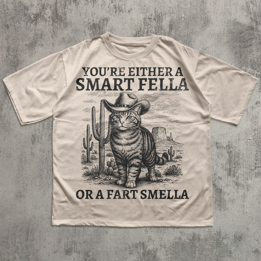 Beige t-shirt with a graphic of a cat in a cowboy hat and text on a textured gray background