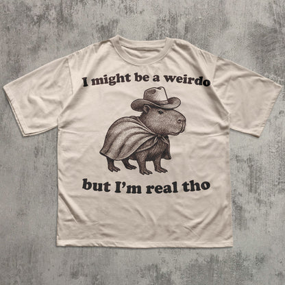 Beige t-shirt with a graphic of a capybara wearing a cowboy hat and cape, with text on a textured gray background.