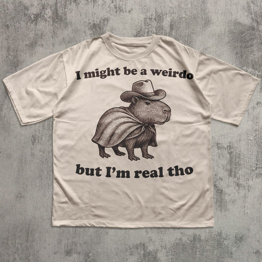 Beige t-shirt with a graphic of a capybara wearing a cowboy hat and cape, with text on a textured gray background.