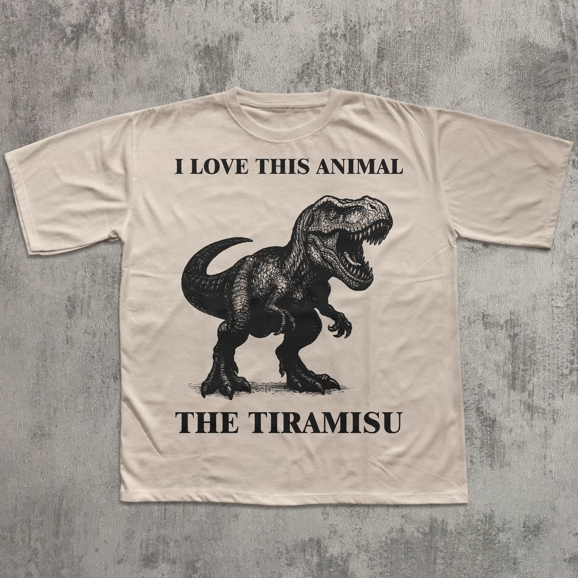 Beige t-shirt with a dinosaur graphic and text on a textured gray background