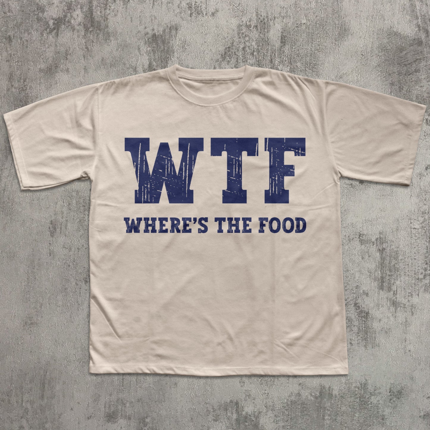 Beige t-shirt with blue text 'WTF WHERE'S THE FOOD' on a textured gray background