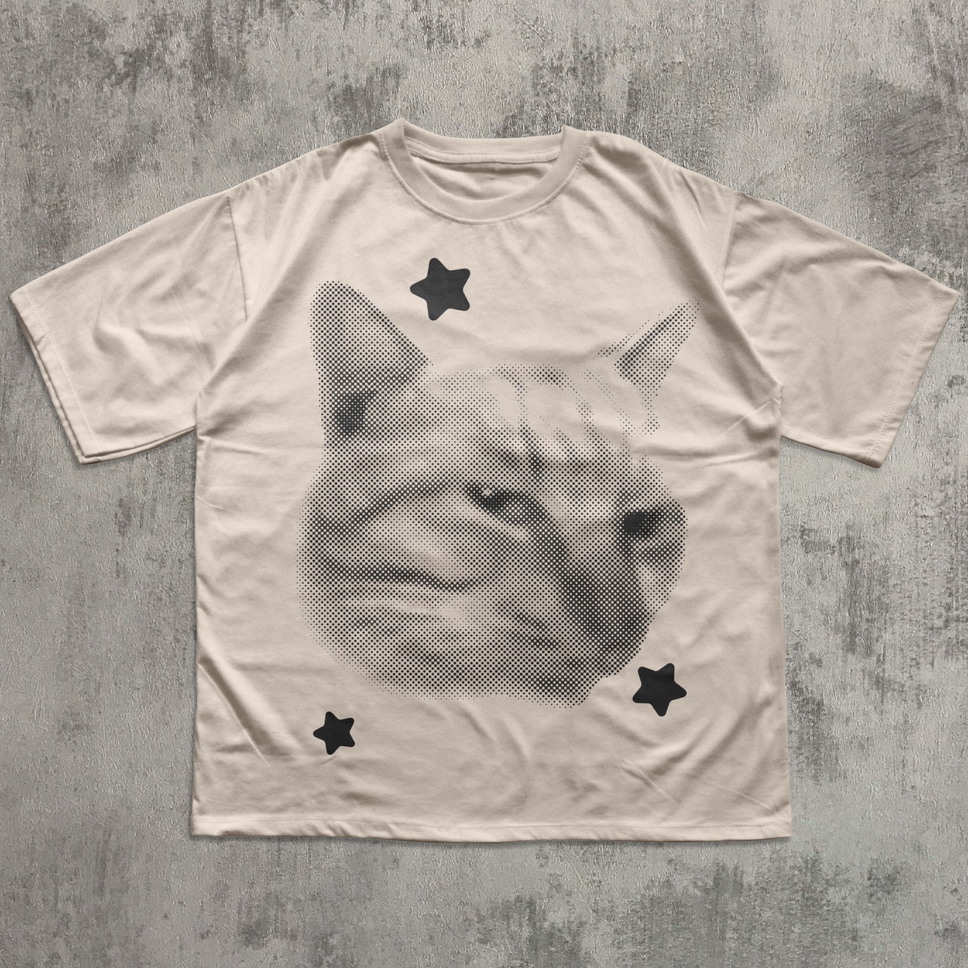 T-shirt with a cat face design and star shapes on a textured gray background