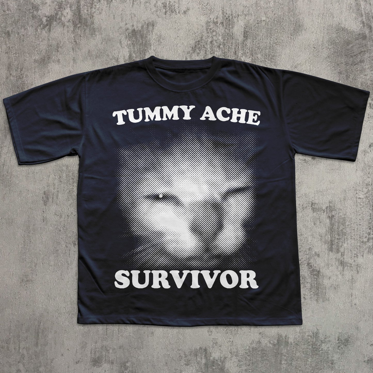 Black t-shirt with a cat face graphic and text 'TUMMY ACHE SURVIVOR' on a textured gray background