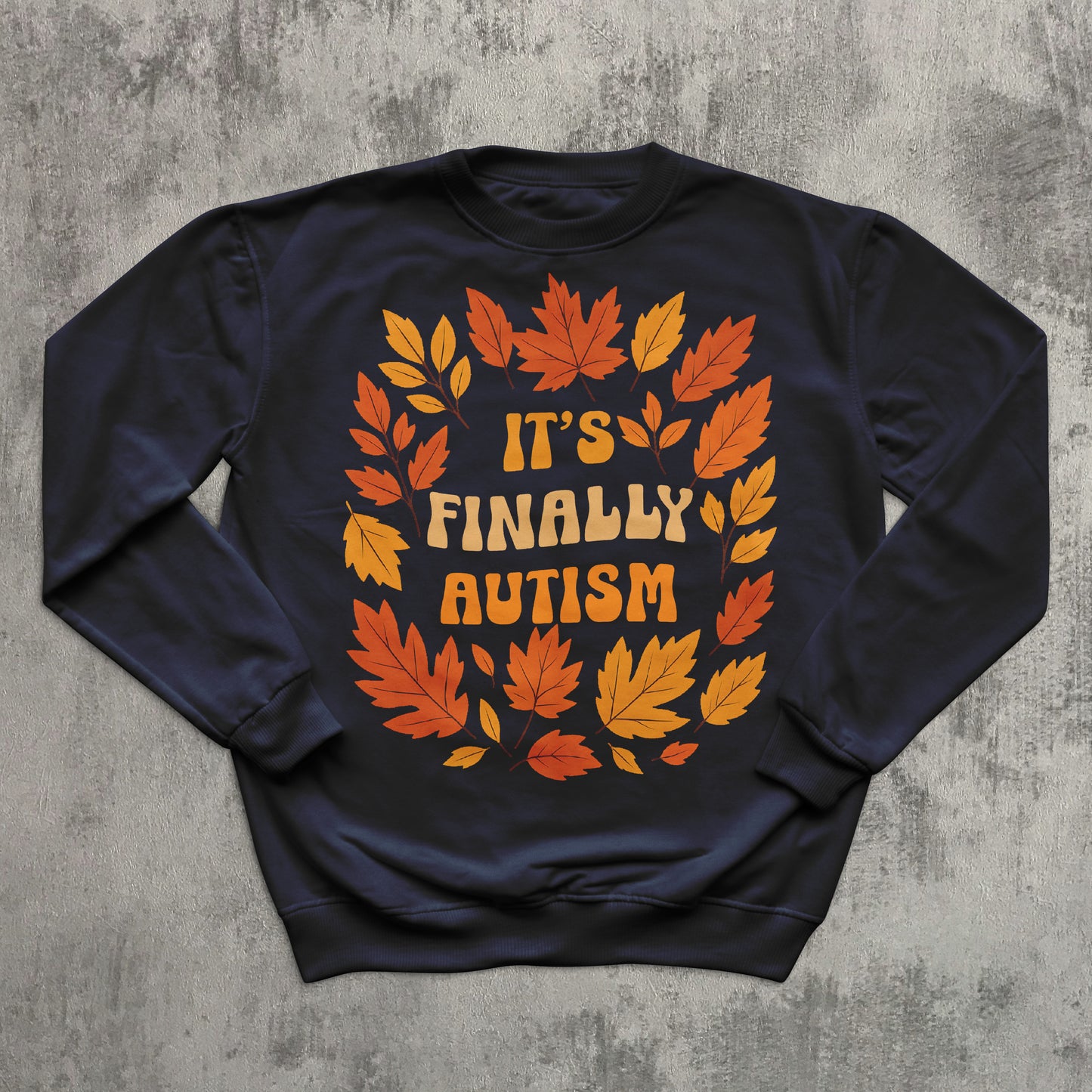 Navy blue sweatshirt with autumn leaf design and 'It's Finally Autism' text on a concrete background