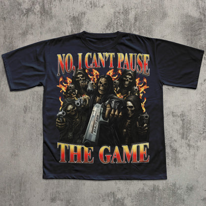 Black t-shirt with graphic design of skeletons holding guns and text 'No, I Can't Pause The Game' on a concrete surface.
